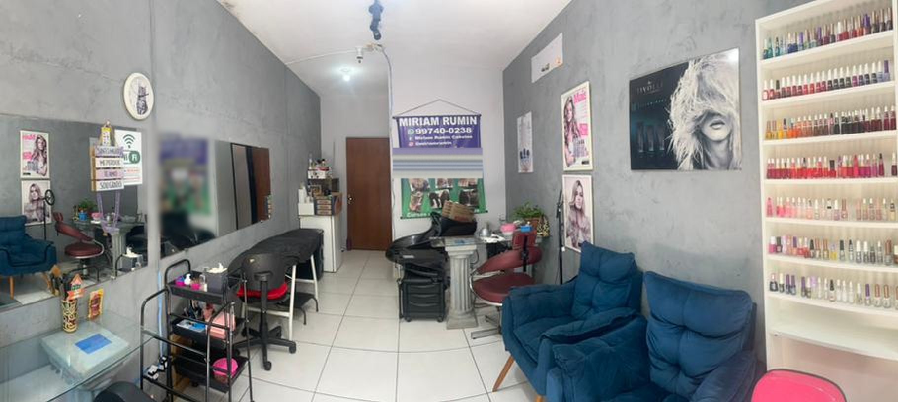Vista panorâmica do interior do salão de beleza, com estações de trabalho, espelhos, poltronas de espera e prateleira de esmaltes