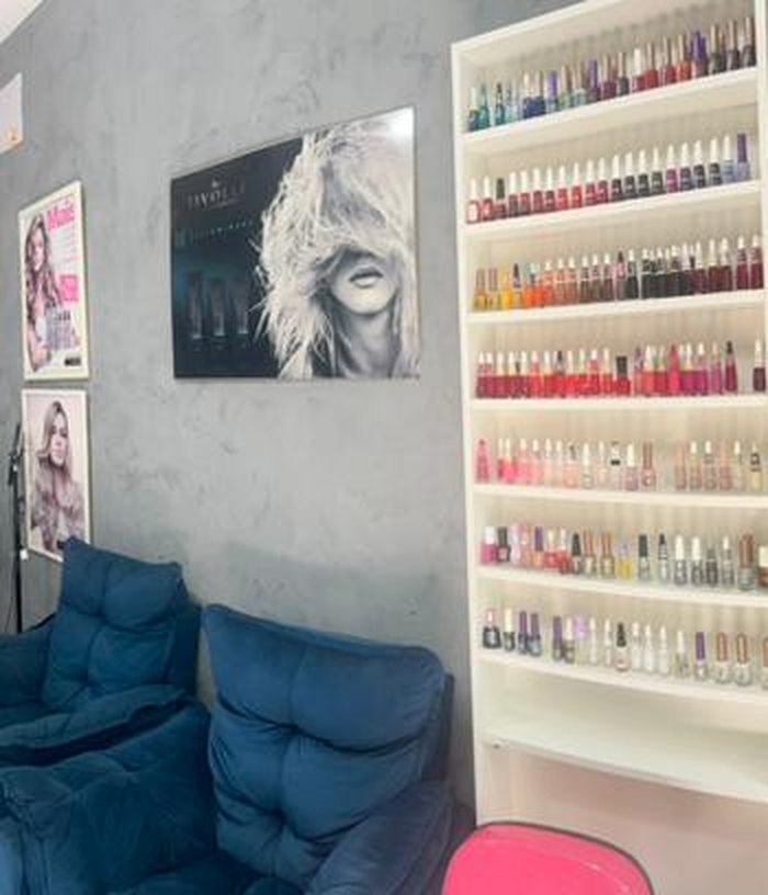 Prateleira branca repleta de esmaltes coloridos ao lado de poltronas azuis de espera
